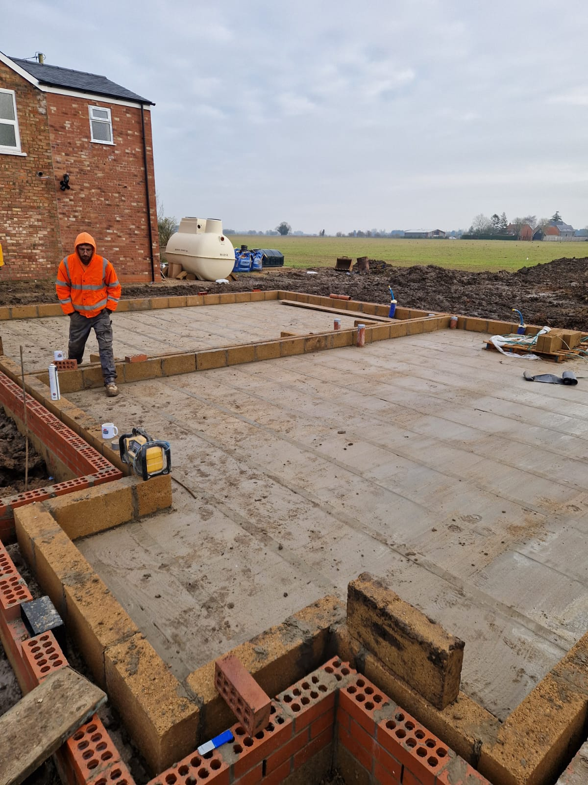 Bricklayer building blockwork foundations on a new-build slab beside a septic tank installation on a Norfolk fen site | new build groundworks in King's Lynn by Humphries Construction